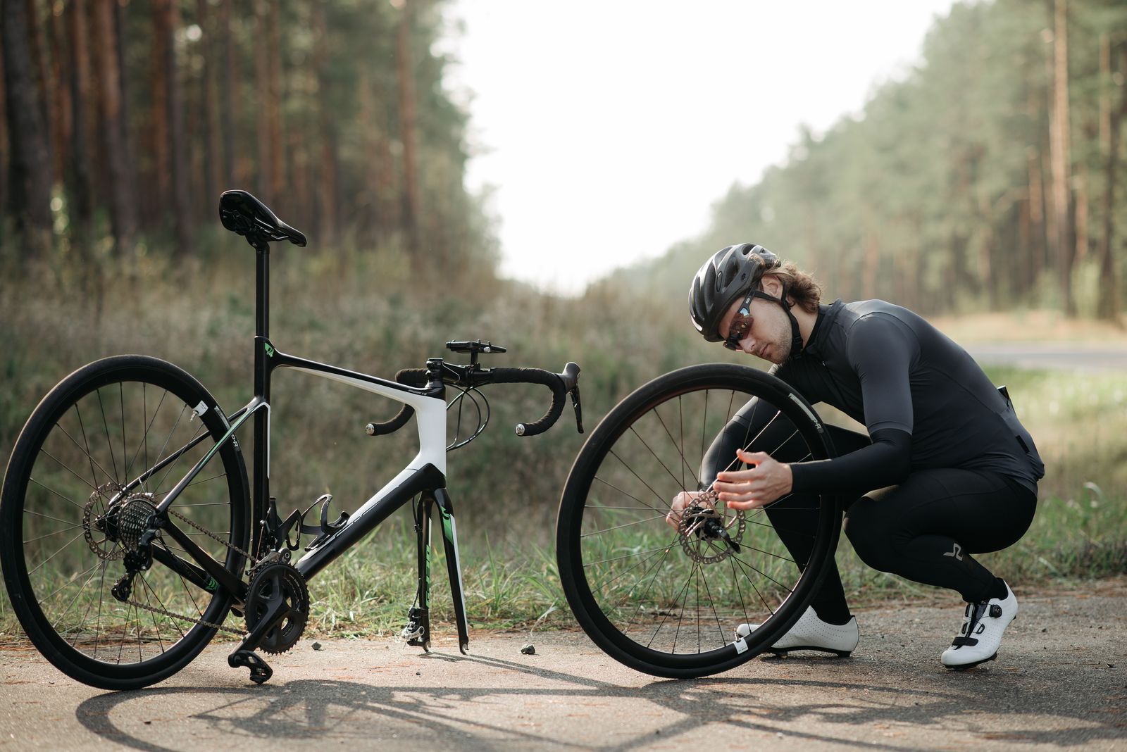 A cyclist crouched beside a road bike, working on the wheel outdoors.