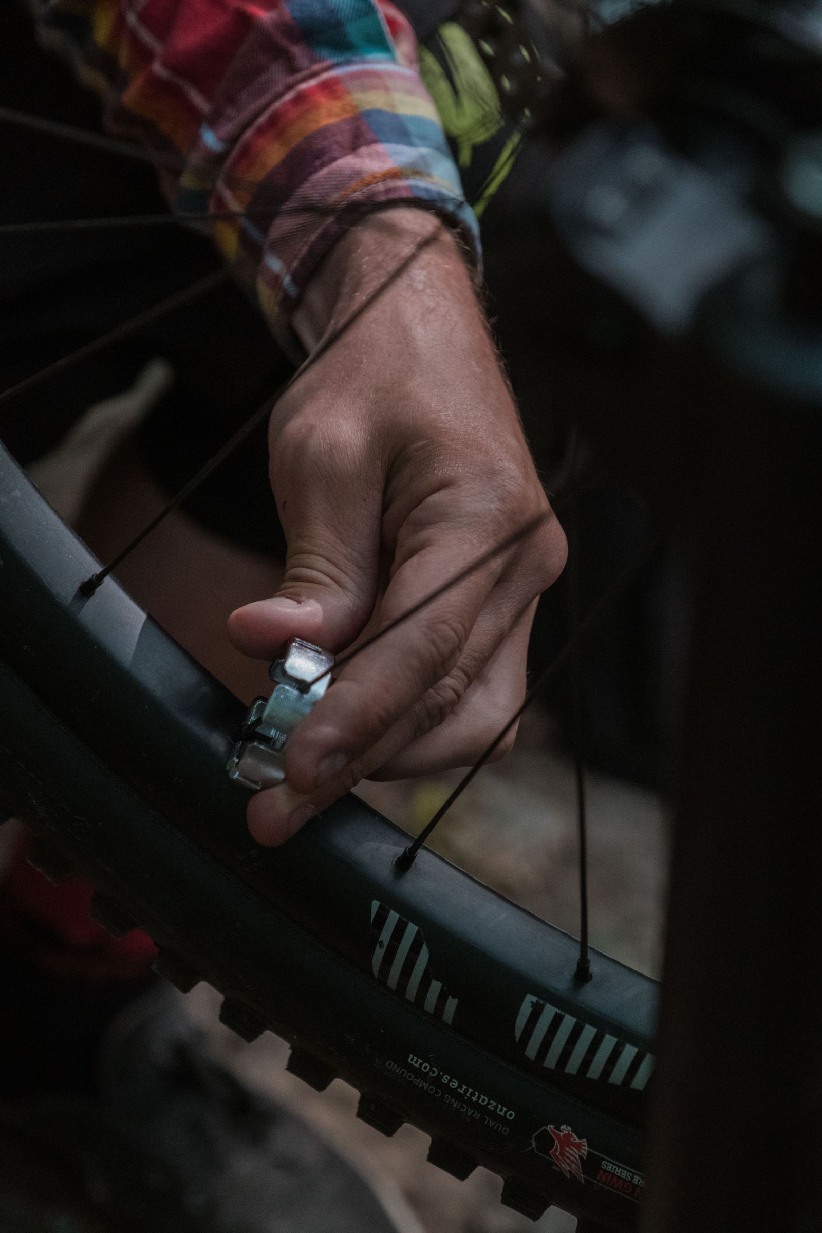 A hand adjusting bicycle wheel spokes with a spoke wrench.